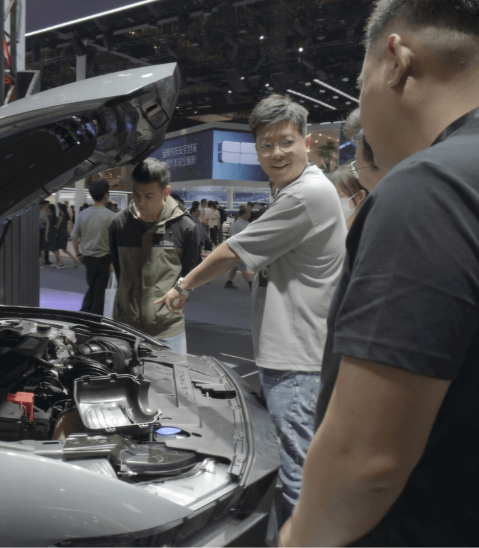 Group of visitors listening to a presenter explain car hardware at a China auto show